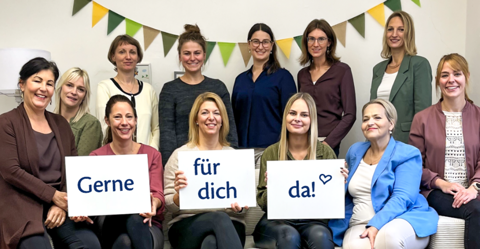 Das Bild zeigt eine Gruppe von zwölf Frauen, die vor einem hellen Hintergrund posieren. Sie halten Schilder mit den Worten "Gerne", "für dich" und "da!" in der Hand.