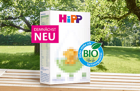 Auf einer Holzfläche mit grünem Gartenhintergrund steht eine Produktbox mit der Aufschrift "DEMNACHST NEU" und einer "BIO"-Zertifizierung.