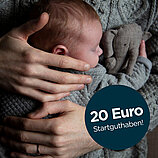 Nahaufnahme eines Babys, das von einem Erwachsenen in den Arm genommen wird, mit einem Plüschtier, das einem Elefanten ähnelt, daneben.