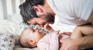 Ein zärtlicher Moment zwischen einem Mann und einem Baby, bei dem sich der Mann hinunterbeugt, um spielerisch mit dem Baby zu spielen.