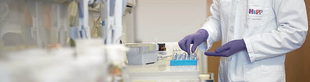 Eine Laborumgebung, in der eine Person in einem weißen Laborkittel mit mehreren blauen Reagenzgläsern hantiert.