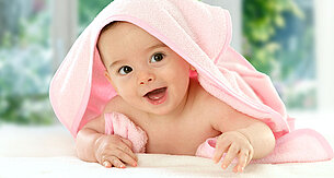 Ein in ein rosa Handtuch gewickeltes Baby, das neugierig in die Kamera schaut.