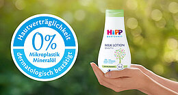 Eine Hand hält eine Flasche eines Babypflegeprodukts mit der Aufschrift "Hipp Baby Sensitive Milk Lotion", die auf den Gehalt von 0 % Mikroplastik und 0 % Mineralöl hinweist.