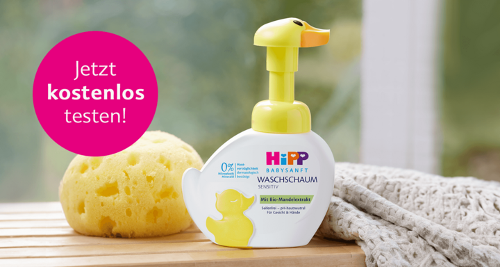 Eine Flasche Babyseife mit der Aufschrift "HiPP" und einem gelben Spender in Form einer Ente, die neben einem gelben Schwamm platziert ist, mit einem rosa Banner im Hintergrund, auf dem "Jetzt kostenlos testen!" steht.