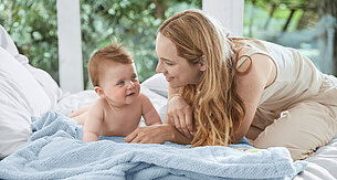 Ein zärtlicher Moment zwischen einer Mutter und ihrem Baby, wobei die Mutter sanft mit dem Kind auf einem Bettchen umgeht.
