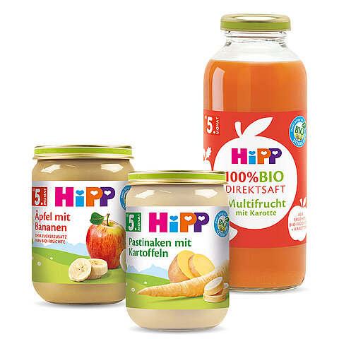 Drei Gläschen Babynahrung, jedes mit einer anderen Frucht und einem Prozentsatz an biologischem Inhalt beschriftet, begleitet von einer Flasche 100% biologischen Fruchtsafts.