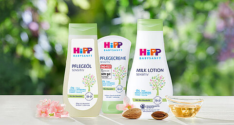Eine Reihe von Babypflegeprodukten von Hipp, darunter eine Körperbutter, ein Massageöl und eine Körperlotion, die alle mit natürlichen Inhaltsstoffen gekennzeichnet sind und vor einer grünen Kulisse präsentiert werden.