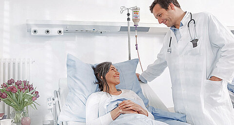 Eine medizinische Fachkraft, die sich um einen Patienten in einem Krankenhauszimmer kümmert, wobei der Schwerpunkt auf der Interaktion und dem Komfort des Patienten liegt.
