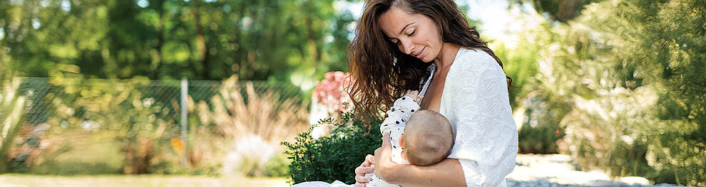 Eine Mutter, die ein Baby an sich drückt, umgeben von einer ruhigen, grünen Umgebung.