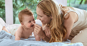 Ein zärtlicher Moment zwischen einer Mutter und ihrem Baby, in dem die Mutter spielerisch das Gesicht des Babys berührt.