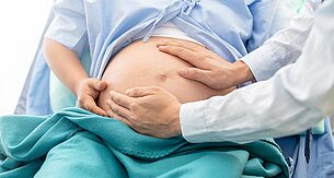 Eine medizinische Fachkraft berührt sanft den Bauch einer schwangeren Frau.