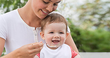 Ein freudiger Moment zwischen einer Mutter und ihrem Baby, bei dem die Mutter ihr Kind mit einem Löffel füttert.