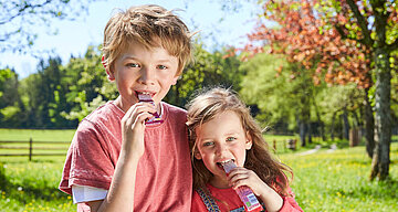 Zwei Kinder, ein Junge und ein Mädchen, im Freien in einem Park, jedes hält einen rosafarbenen Snack in der Hand und isst ihn.
