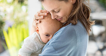 Ein zärtlicher Moment zwischen einer Frau und einem Baby, wobei die Frau das Baby sanft an ihr Gesicht drückt.