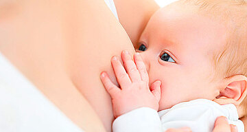 Ein Baby, das seine Hand auf die Brust der Mutter legt und zu säugen scheint.