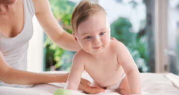 Ein Baby, das scheinbar krabbelt, und eine Frauenhand, die sanft seinen Rücken berührt.