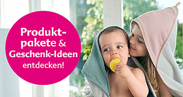 Ein kleines Kind, vermutlich ein Baby, eingewickelt in ein Handtuch, mit einem gelben Gegenstand im Mund, während ein älteres Kind, vermutlich ein Geschwisterkind, die Stirn des Babys küsst.