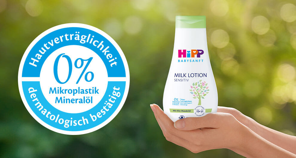 Eine Hand hält eine Flasche eines Babypflegeprodukts mit der Aufschrift "Hipp Baby Sensitive Milk Lotion", die auf den Gehalt von 0 % Mikroplastik und 0 % Mineralöl hinweist.