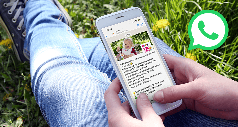Ein Handybildschirm, der eine Werbung für ein Babyprodukt anzeigt, mit einer Frau, die im Gras sitzt, und einem grünen WhatsApp-Logo im Hintergrund.
